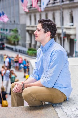 Genç yakışıklı bir adam dışarıda dinlenmek için oturuyor. Arka planda Amerikan bayrakları asılı..