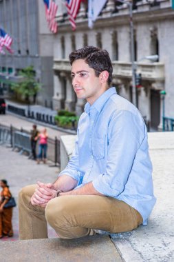 Omzunu silkerken, genç yakışıklı bir adam dışarıda sahnede rahatlamak için oturuyor. Arka planda Wall Street tabelası var..