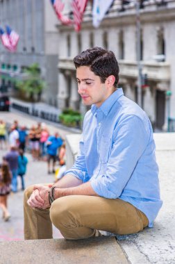 Ellerini kıskaçlıyor ve başını eğiyor, genç yakışıklı bir adam dışarıda sahnede oturuyor, rahatlıyor ve düşünüyor. Arka planda Amerikan bayrakları asılı..