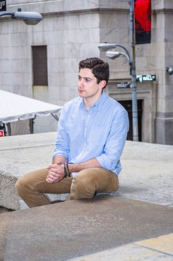 Ellerini kenetliyor ve ileriye bakıyor, genç yakışıklı bir adam caddenin köşesinde oturuyor, rahatlıyor ve düşünüyor..