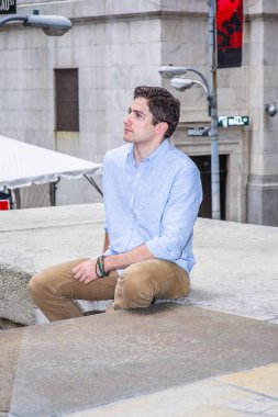 Genç yakışıklı bir adam sokağın köşesindeki bir sahnede oturuyor, rahatlıyor ve düşünüyor..