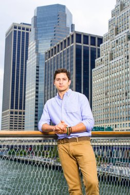 Açık mavi gömlekli ve koyu sarı kotlu genç yakışıklı bir adam bir iş yerinin önünde duruyor ve sana bakıyor..