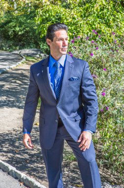 Mavi bir takım elbise, mavi gömlek ve mavi desenli kravat giyen güçlü bir iş adamı dışarıda duruyor ve derin düşüncelere dalıyor..