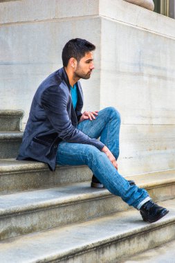 Koyu mor yün ceket ve mavi kot pantolon giyen, küçük bir ekmek ve bıyıklı genç yakışıklı bir adam ofis binasının dışındaki basamaklarda oturuyor, rahatlıyor ve düşünüyor..