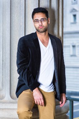 Siyah yün ceket, beyaz iç çamaşırı ve koyu sarı pantolon giyen, gözlük takan, ekmek ve bıyıklı genç bir profesyonel nedense bir sütunun yanında durup düşünceli bir şekilde sana bakıyor.