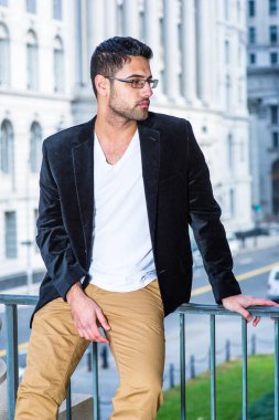 Siyah yün ceket, beyaz iç çamaşırı ve koyu sarı pantolon giyen, gözlük takan, ekmek ve bıyıklı genç bir profesyonel, nedense korkulukların yanında oturup dinleniyor ve düşünüyor.