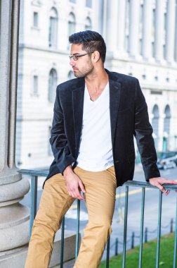 Siyah yün ceket, beyaz iç çamaşırı ve koyu sarı pantolon giyen, gözlük takan, ekmek ve bıyıklı genç bir profesyonel, gelişigüzel bir şekilde trabzanın kenarında oturup, dinlenmek ve düşünmek.