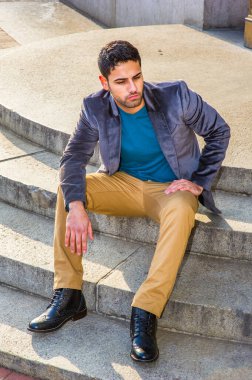 Koyu mor yün ceket, koyu sarı pantolon ve deri ayakkabı giyen, ekmek ve bıyıklı genç bir Orta Doğulu, daire basamaklarında oturuyor, rahatlıyor ve düşünüyor.