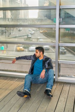 Ekmek ve bıyıklı genç bir adam yerde oturuyor ve düşünüyor. Arka plan bir sokak ve bir sürü araba.