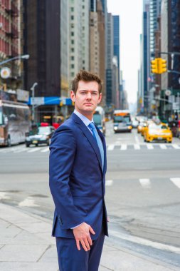 Dressing in a blue slim fit suit and patterned tie, a young handsome businessman is standing on a busy street in a big city