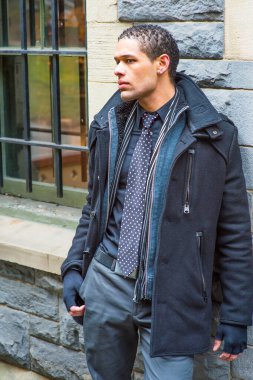 Dressing in a pea coat, tie and gloves, a young handsome guy is waiting outside by the windo