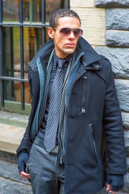 Dressing in a pea coat, tie and gloves, wearing sunglasses, a young guy is waiting outside by the windo