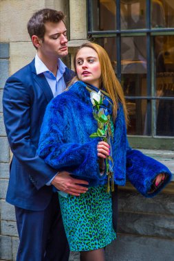 Holding a white flower, a attractive young couple is passionately looking at each other by a window