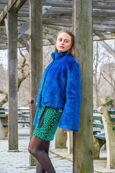 青いフェイクファー サイズのジャケット パターン化されたドレスでドレッシング かわいい女の子は冬の木製フレーム構造の柱に対して傾いている 悲しい 楽しみにして — ストック写真