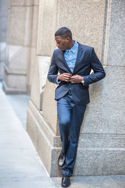 Başını eğerek, genç bir siyahi işadamı dışarıda duruyor ve derin düşüncelere dalıyor.