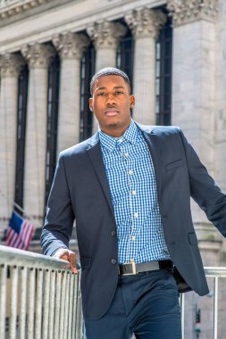 Genç bir siyah işadamı bir ofis binasının önünde duruyor ve kendinden emin bir şekilde savaş arıyor.