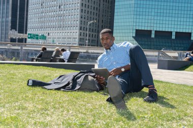 Genç bir zenci iş bölgesinde çimlerde uzanıyor ve ders çalışıyor.