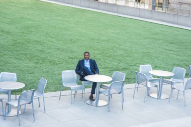 Genç yakışıklı bir siyah adam yeşil çimlerin yanında bir sandalyede oturuyor ve seni bekliyor.