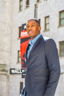 Genç bir siyah işadamı dışarıda duruyor, kendinden emin bir şekilde ileriye bakıyor. Arka planda Wall Street tabelası var.
