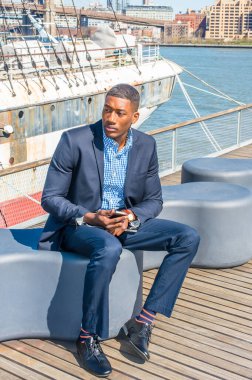 Mavi takım elbise, deri ayakkabılar, cep telefonu ve tablet bilgisayar taşıyan genç bir siyah işadamı güvertede seni bekliyor. Arka plan bir liman.