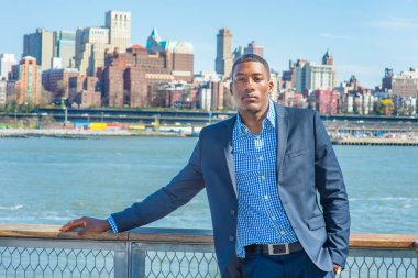 Genç bir siyah işadamı nehrin kenarında duruyor, ileriye bakıyor. Arka plan eski bir şehir manzarasıdır.