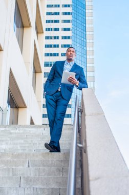 Bir tablet bilgisayar tutuyor, tırabzana yaslanıyor, genç, yakışıklı bir siyah işadamı bir iş binasının önünde duruyor, okuyor, düşünüyor ve çalışıyor.