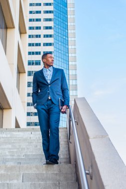 Elinde bir tablet bilgisayar olan yakışıklı bir iş adamı bir iş binasının önünde kendinden emin bir şekilde bekliyor.