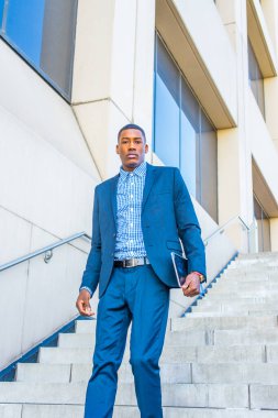 Bir tablet bilgisayar taşıyan genç, yakışıklı bir siyahi işadamı güvenli bir şekilde bir iş binasının merdivenlerinden aşağı iniyor.