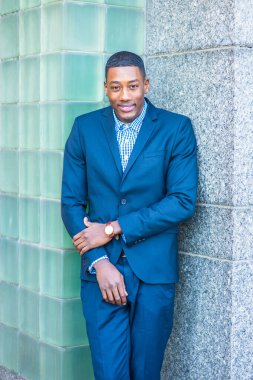 Genç yakışıklı siyah bir adam iki duvarın arasında duruyor, gülümsüyor.