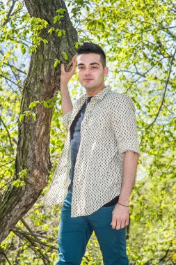 Genç yakışıklı bir adam bahar mevsiminin sabahında bir ağacın yanında duruyor.