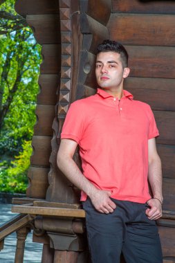 Kırmızı Polo tişörtü giymiş genç yakışıklı bir adam eski bir stilin yanında duruyor, ahşap kapı aralığı, düşünceli bir şekilde sana bakıyor.