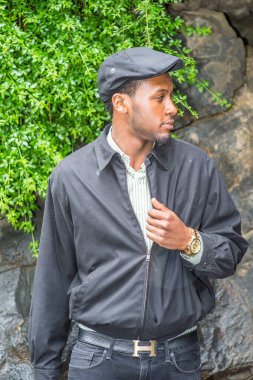 Su geçirmez bir ceket, sarmaşık şapkası ve genç yakışıklı bir zenci yağmurlu bir günde yeşil bitkilerle kayaların yanında seni bekliyor.