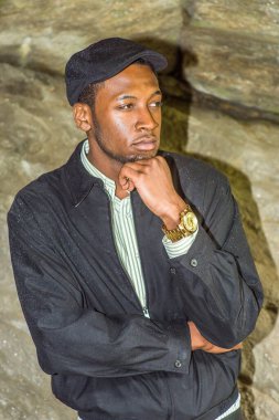 Su geçirmez bir ceket, sarmaşık şapkası ve kayaların yanında duran yakışıklı bir zenci bir eli çenesine dokunarak derin düşüncelere dalıyor. Onun giysileri yağmurdan ıslandı..