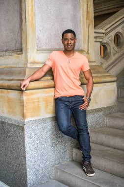 Bir sütuna yaslanmış, genç yakışıklı siyah bir adam merdivenlerde duruyor ve sana gülümsüyor.