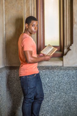Genç yakışıklı siyah bir öğrenci pencerenin yanında duruyor, kitap okuyor.