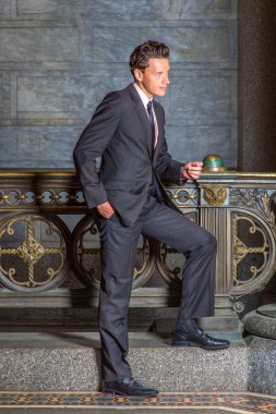 Siyah çizgili bir ceket, pantolon, kravat, deri ayakkabılar, bir eli cebe sokan genç bir işadamı, eski moda bir korkuluğun önünde duruyor, ileriye bakıyor ve düşünüyor.