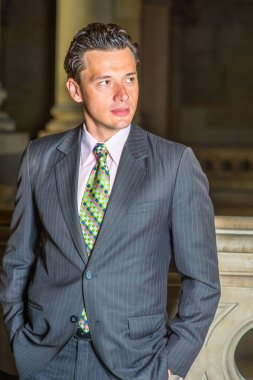 Resmi giyinen ve ceplerini dolduran iki eli olan genç bir işadamı, ofis koridorunda duruyor ve kendinden emin bir şekilde ileriye bakıyor.