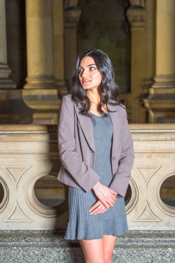 Gri örgü elbise ve ceket giyen genç bir iş kadını ofis koridorunda seni bekliyor.