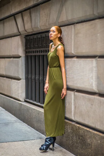 Woman Relaxing on Street. Dressing in a green, long Maxi Tank Dress,  black dress sandals, a young black lady is standing by old fashion style window and wall,  looking up, lost in thought.