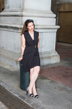 Siyah kolsuz giysiler içinde, güzel bir kadın dışarıda oturuyor, dikkatlice yukarı bakıyor.