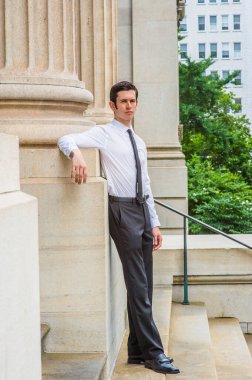 Uzun kollu beyaz gömlek, siyah pantolon, deri ayakkabı, siyah kravat, genç bir katman bir ofis binasının önünde duruyor, dinleniyor ve düşünüyor.