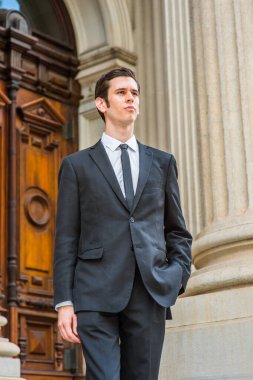 Resmi olarak siyah bir takım elbise, siyah bir kravat, bir elini cebine sokan genç bir işadamı bir ofis binasının önünde kendinden emin bir şekilde bekliyor.