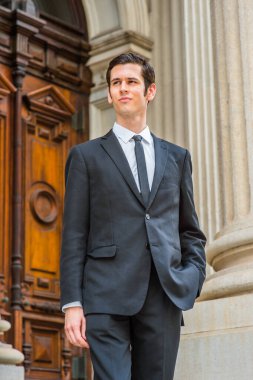 Resmi olarak siyah bir takım elbise, siyah bir kravat, bir elini cebine sokan genç bir işadamı bir ofis binasının önünde kendinden emin bir şekilde bekliyor.