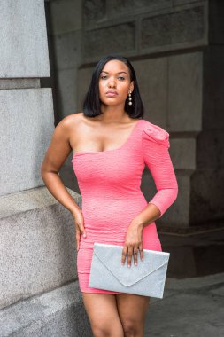 Pembe bir omuz elbisesi ve bir klasör taşıyan siyah bir genç kız dışarıda bekliyor.