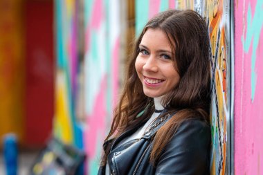 Duvara karşı duran, grafiti püskürten ve kameraya bakan pozitif genç bir kız.