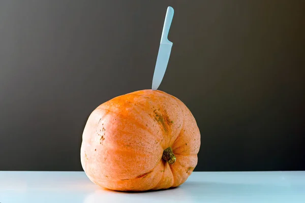 huge orange pumpkin with a knife stabbed in the side to demonstrate a pumpkin carving theme