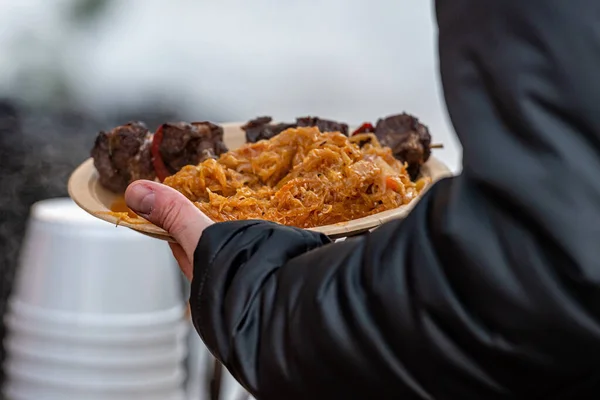 stewed cabbage with sausages - a traditional dish at the annual Christmas market, hands holding a plate of hot food, close-up, soft focus