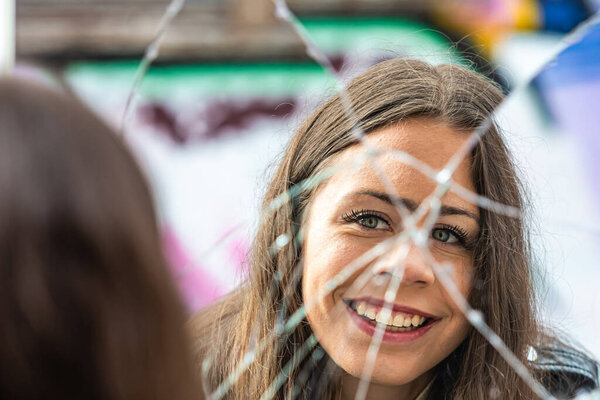 a young, positive woman looks at her reflection in a broken mirror