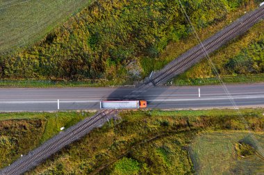 Kırsal bölgedeki arabalarla asfalt yolu geçen demiryolu raylarının hava görüntüsü.