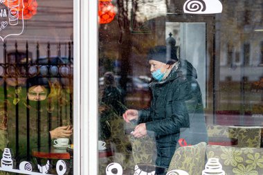 Riga, Letonya - 6 Kasım 2020: Coronavirüs salgını sırasında bir kafede tıbbi yüz maskesi takan insanlar, covid-19 virüsünün yayılması ile mücadele eden bir konsept, pencereden bakan bir bakış.